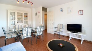 Ein Wohnzimmer mit Esstisch, Stühlen, einem Fernseher auf einem Schrank und einer Vitrine.
