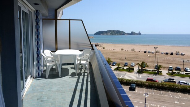 Ein Balkon mit Tisch und Stühlen mit Blick auf Strand und Parkplatz.