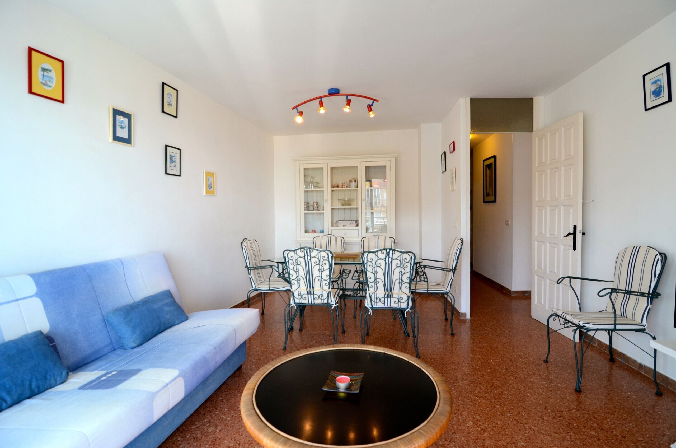A living room with a sofa, a coffee table, and a dining area with chairs and a cabinet.