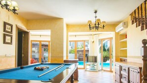 Una mesa de billar en una habitación con vistas a una piscina, un televisor y un mueble de madera.