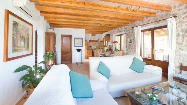 A spacious living room with wooden beams, white sofas with teal cushions, a glass coffee table, and a stone wall. - Pollensa retreat, walk to Old Town and 6km to beach! (Palma de Mallorca)