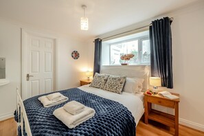 A neatly arranged bedroom with a bed, bedside tables, a window with curtains, and a wall-mounted light fixture.