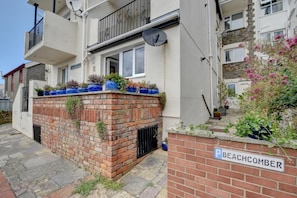 A residential building with a brick wall, potted plants, and a sign reading 'BEACHCOMBER'. - 2 Bed in Woolacombe (oc-beac4) (Woolacombe)