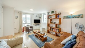 A living room with a sofa, a coffee table, a bookshelf, a television, and a floor lamp. - 2 Bed in Woolacombe (oc-beac4) (Woolacombe)