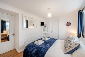 A bedroom with a bed, a bedside table, a mirror, a TV, and a door. - 2 Bed in Woolacombe (oc-beac4) (Woolacombe)