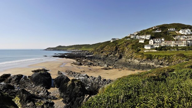 A coastal landscape with a sandy beach, rocky shoreline, and houses on a hillside. - 2 Bed in Woolacombe (oc-beac4) (Woolacombe)