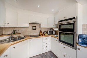 A compact kitchen with white cabinets, a double oven, a microwave, and a Bosch water dispenser. - 2 Bed in Woolacombe (oc-beac4) (Woolacombe)