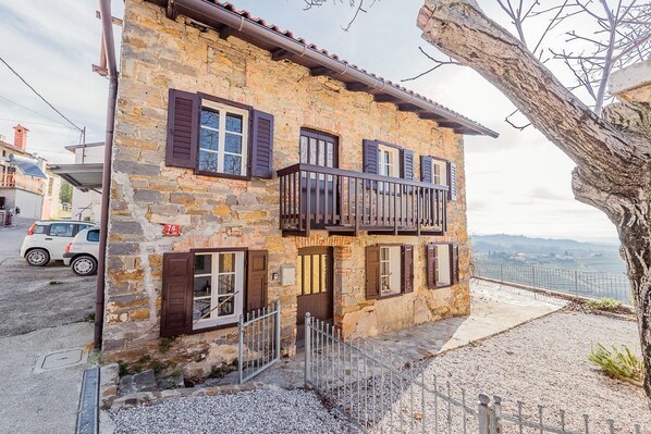 A stone building with a balcony, a gravel driveway, and a view of the landscape.