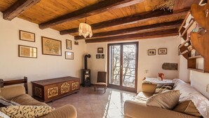 A cozy living room with wooden beams, a fireplace, a sofa, and a dining table. - Little Vista, Smartno, Goriska Brda - 2 Bedroom Holiday House (Kojsko)