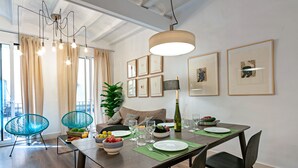 A dining area with a wooden table set for four, surrounded by chairs. There are framed pictures on the wall, a potted plant, and a hanging light fixture. - Born - Habitat Apartments (Barcelona)
