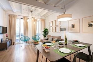 A modern dining area with a wooden table set for two, a sofa, and a television in the background. - Born - Habitat Apartments (Barcelona)