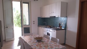 Eine Küche mit weißen Schränken, einer gefliesten Spritzschutzwand und einem Esstisch mit Blumenmuster-Tischdecke.