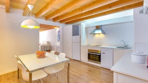 Une cuisine moderne avec des meubles blancs, un coin repas doté d’une table et de chaises blanches, et des poutres en bois au plafond.