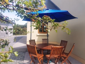An outdoor dining area with a round table and six wooden chairs, shaded by a blue umbrella. - White Thorn House (Clifden)