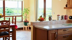 A kitchen with wooden cabinets, a dining table with chairs, a potted plant, and a fruit bowl.