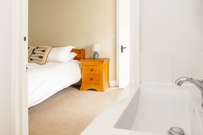 A bedroom with a bed, a wooden nightstand with a lamp, and a white bathtub.