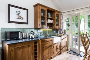 A kitchen with wooden cabinets, a microwave, a kettle, and a sink.