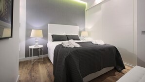 Een moderne hotelkamer met een groot bed, twee nachtkastjes met lampen, een grijze accentmuur en een houten vloer.