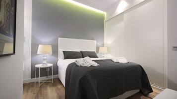Una habitación de hotel moderna con una cama grande, dos mesitas de noche con lámparas, una pared de acento gris y suelo de madera.