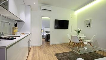 Una cocina moderna con horno integrado, un comedor con mesa de vidrio y un espacio de sala con televisor de pantalla plana.
