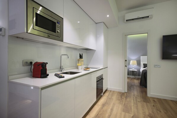 A modern kitchen with white cabinets, a stainless steel microwave, a red kettle, and a sink.