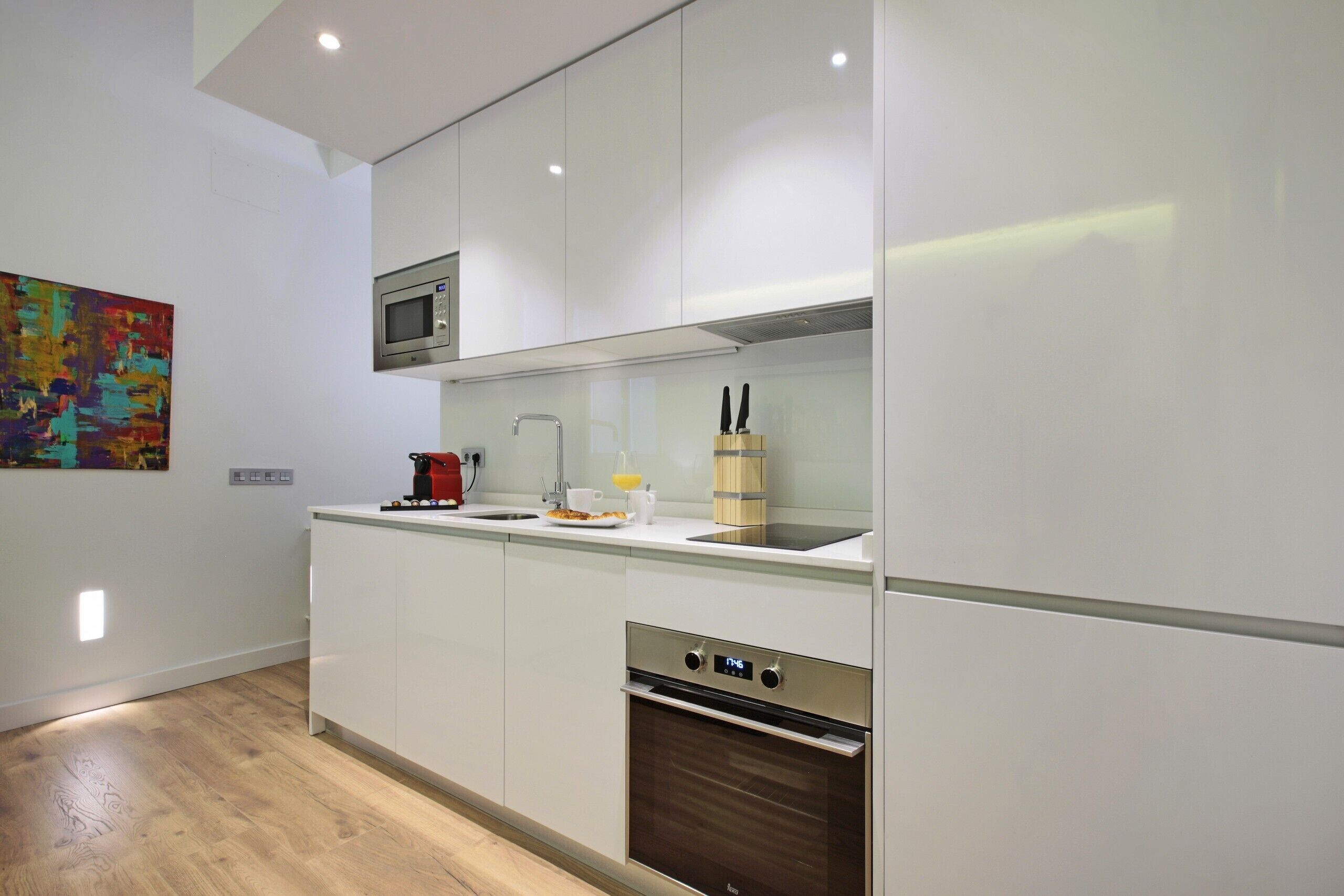 Una cocina moderna con armarios blancos, microondas integrado, horno de acero inoxidable y tabla de cortar de madera con cuchillos.