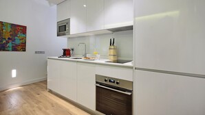 Een moderne keuken met witte kasten, een ingebouwde magnetron, een roestvrijstalen oven en een houten snijplank met messen.