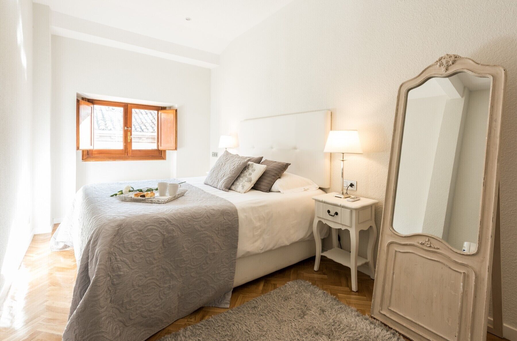 Een slaapkamer met een bed, nachtkastje, lamp en een grote spiegel.