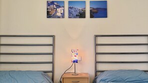 Un dormitorio con dos camas, una mesita de noche con una lámpara y tres cuadros enmarcados en la pared.