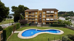 Un edificio de dos pisos con piscina rodeada por un borde de piedra y un césped.