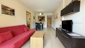 Una sala de estar con un sofá rojo, una mesa de centro de madera, un televisor sobre un mueble negro y un área de comedor al fondo.