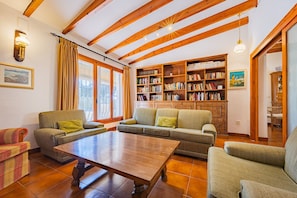 A cozy living room with wooden beams, a fireplace, a bookshelf, and a dining area.