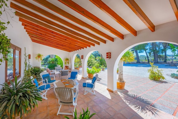 An outdoor patio with wooden beams, blue chairs, and potted plants.