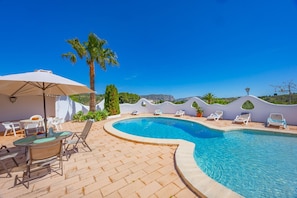 A pool area with lounge chairs, a table, and a palm tree.