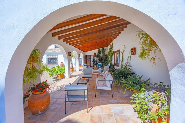 Um pátio externo com mesas, cadeiras, uma pérgola e plantas em vasos.