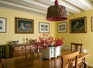 A dining area with a wooden table, chairs, a vase with red flowers, and framed artworks on the wall.