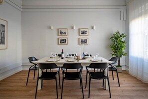 A dining room with a white table set for six, black chairs, framed pictures on the wall, and a potted plant. - Elegant Central Apartment Bailen Comfort (Barcelona)
