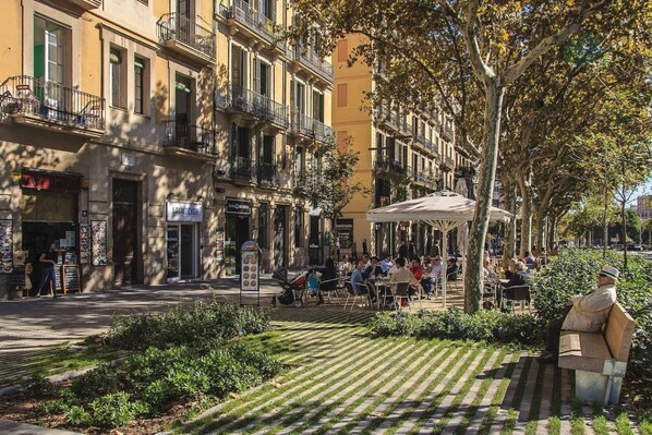 Un carrer amb terrasses a l'exterior, edificis amb balcons i un café.