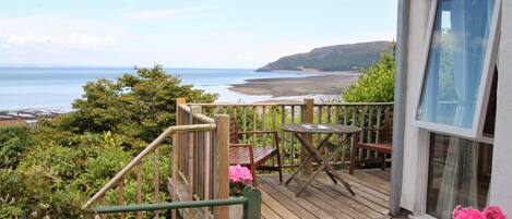A wooden deck with a table and chairs, overlooking a beach and ocean.