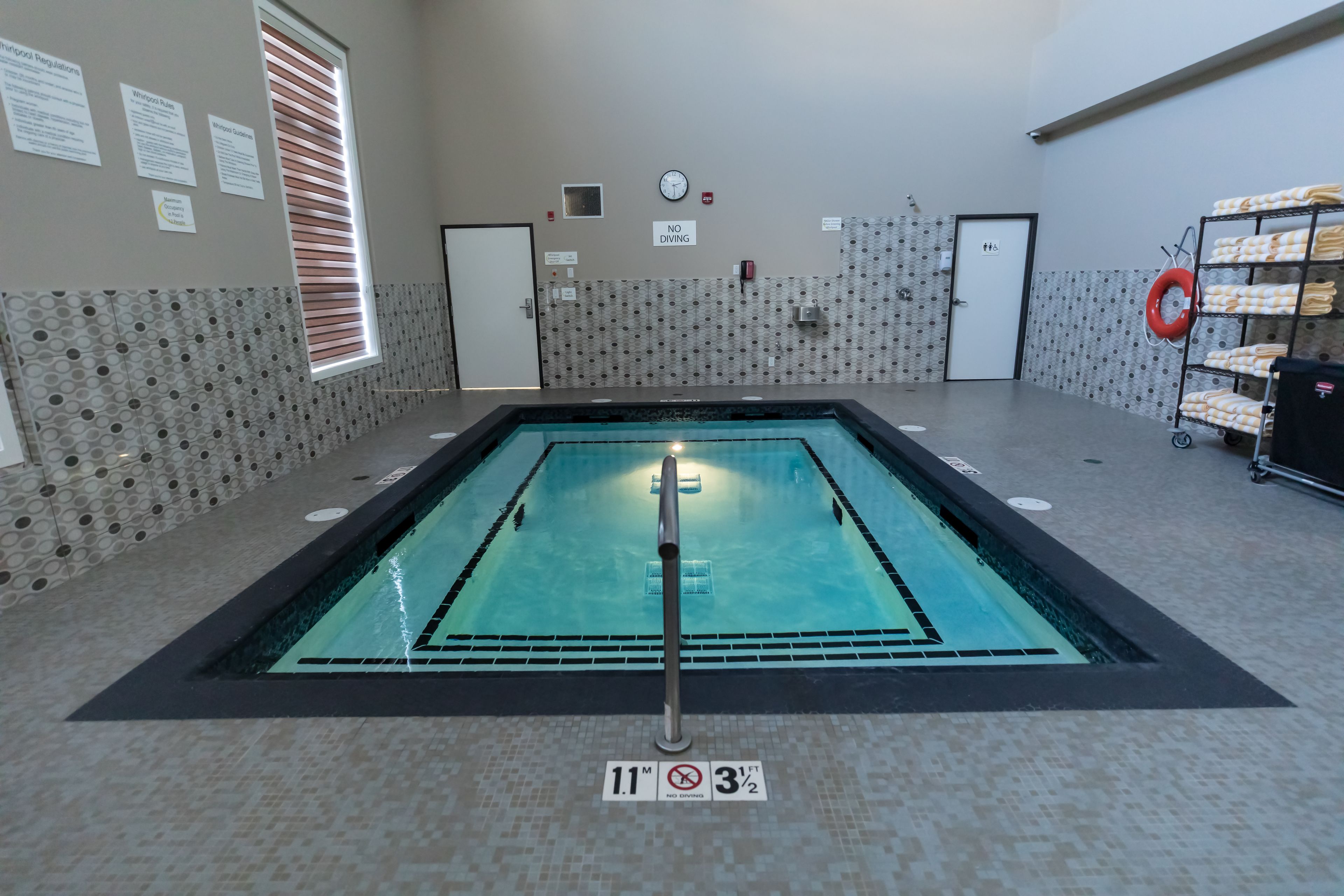 An indoor swimming pool with a tiled floor, a pool ladder, and a no diving sign.
