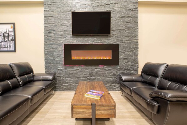 A modern living room with a stone wall, a flat-screen TV, a fireplace, and two leather sofas. - Super 8 by Wyndham Canmore (Canmore)