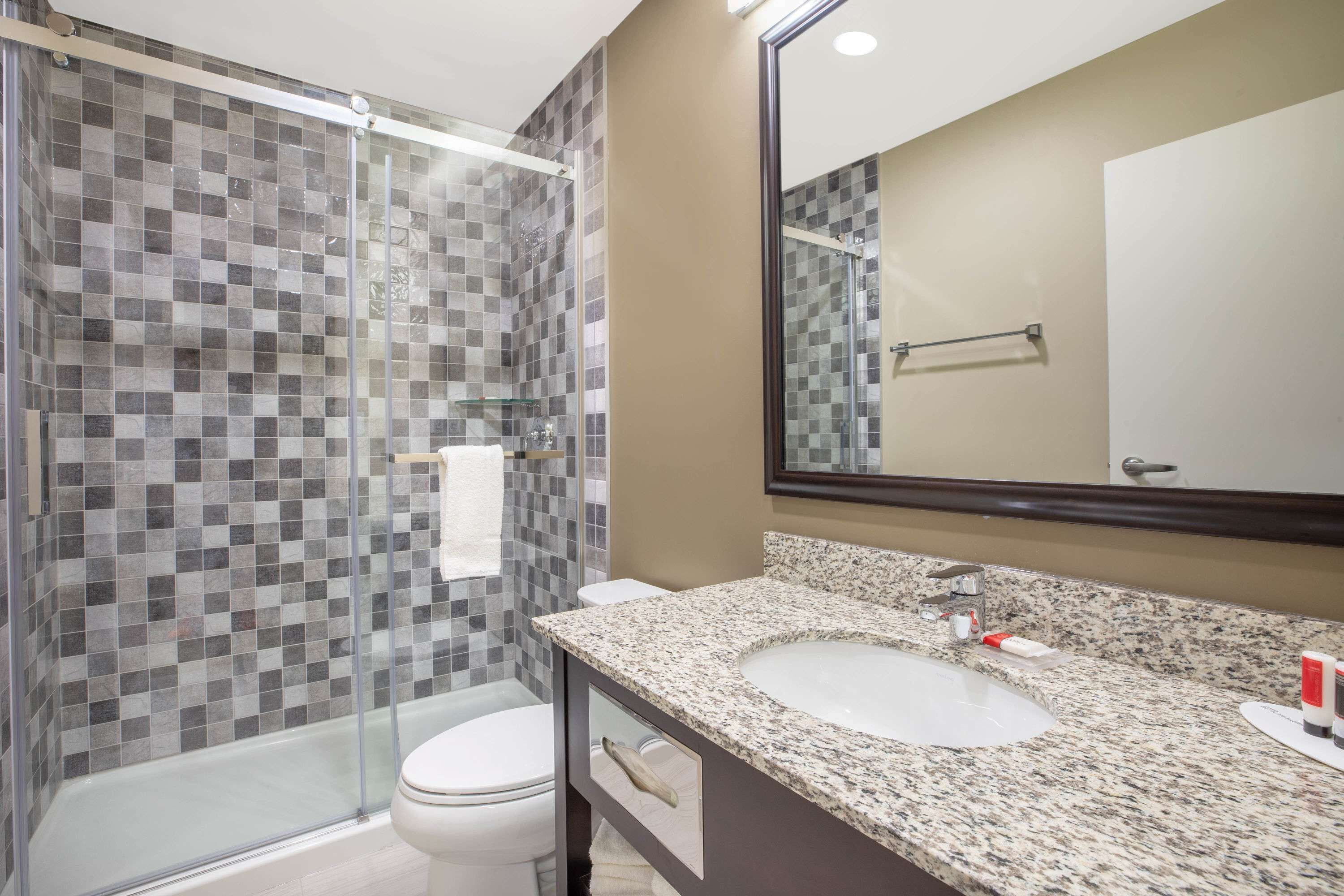Een moderne badkamer met een douchecabine van glas, een wit toilet en een wastafel met een granieten blad.