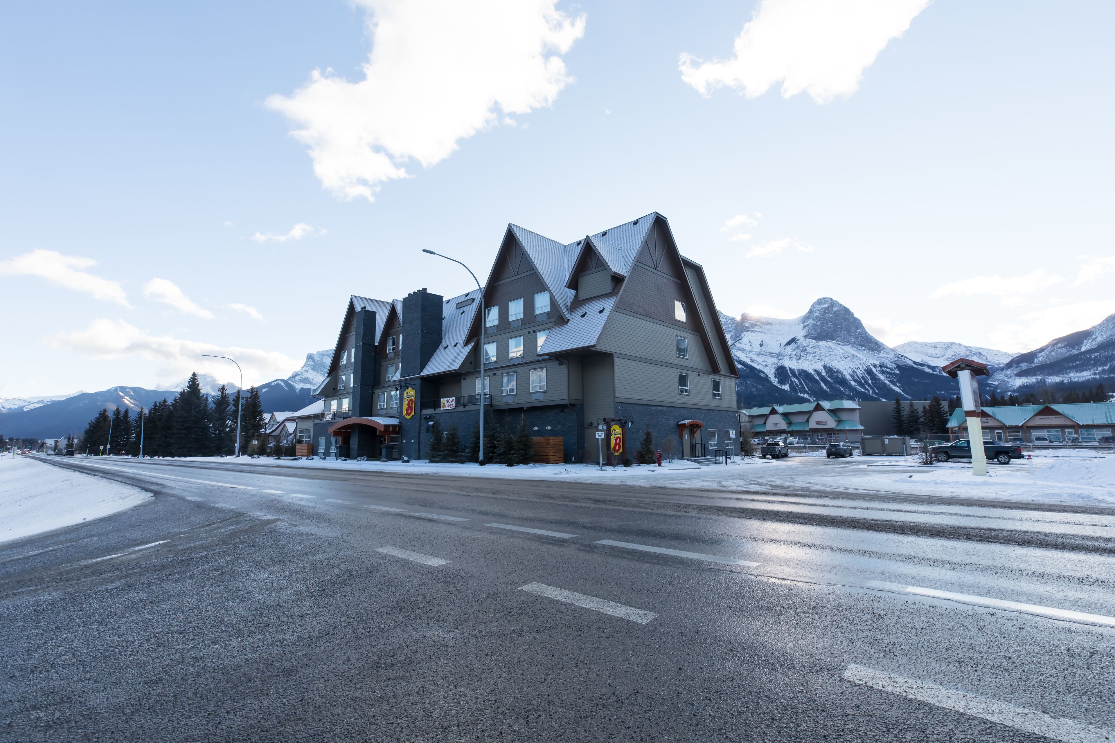 Un edificio moderno con un diseño de techo triangular único, situado cerca de una carretera cubierta de nieve con montañas al fondo.