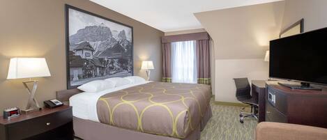 A hotel room with a bed, two bedside tables with lamps, a flat-screen TV, a desk with a chair, and a large framed picture on the wall.
