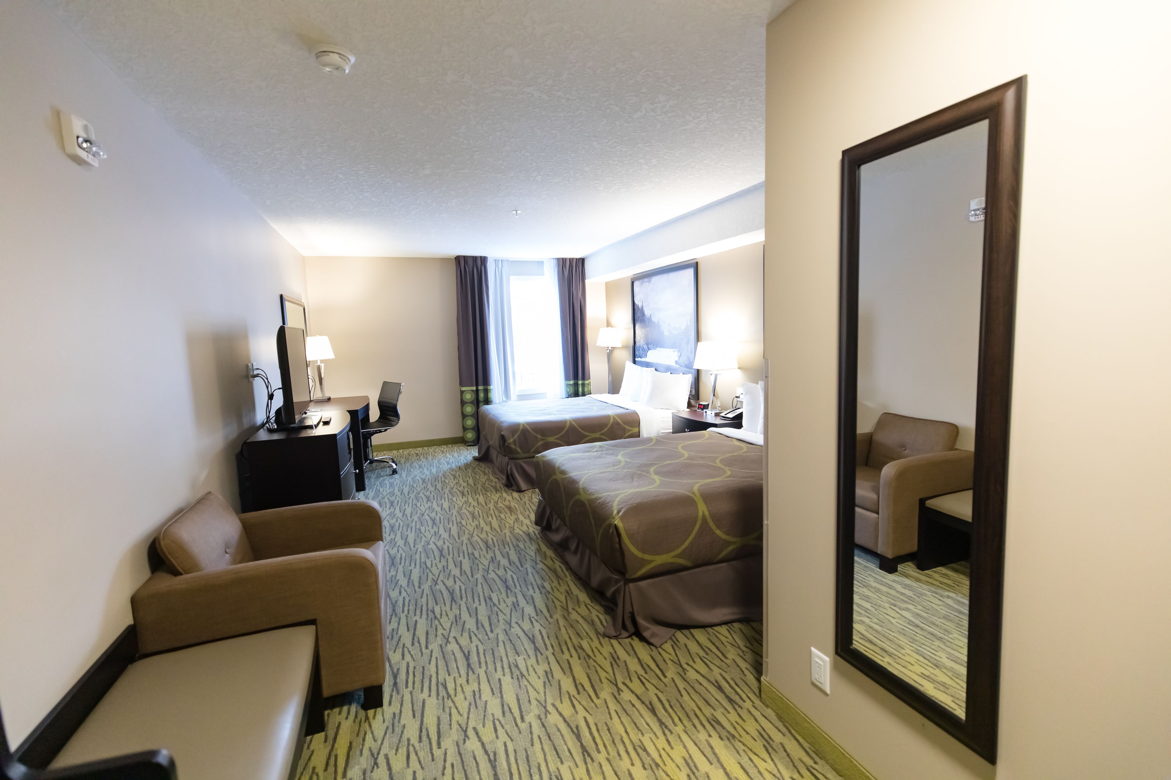 Habitación de hotel con dos camas, un escritorio, una silla y un espejo grande.