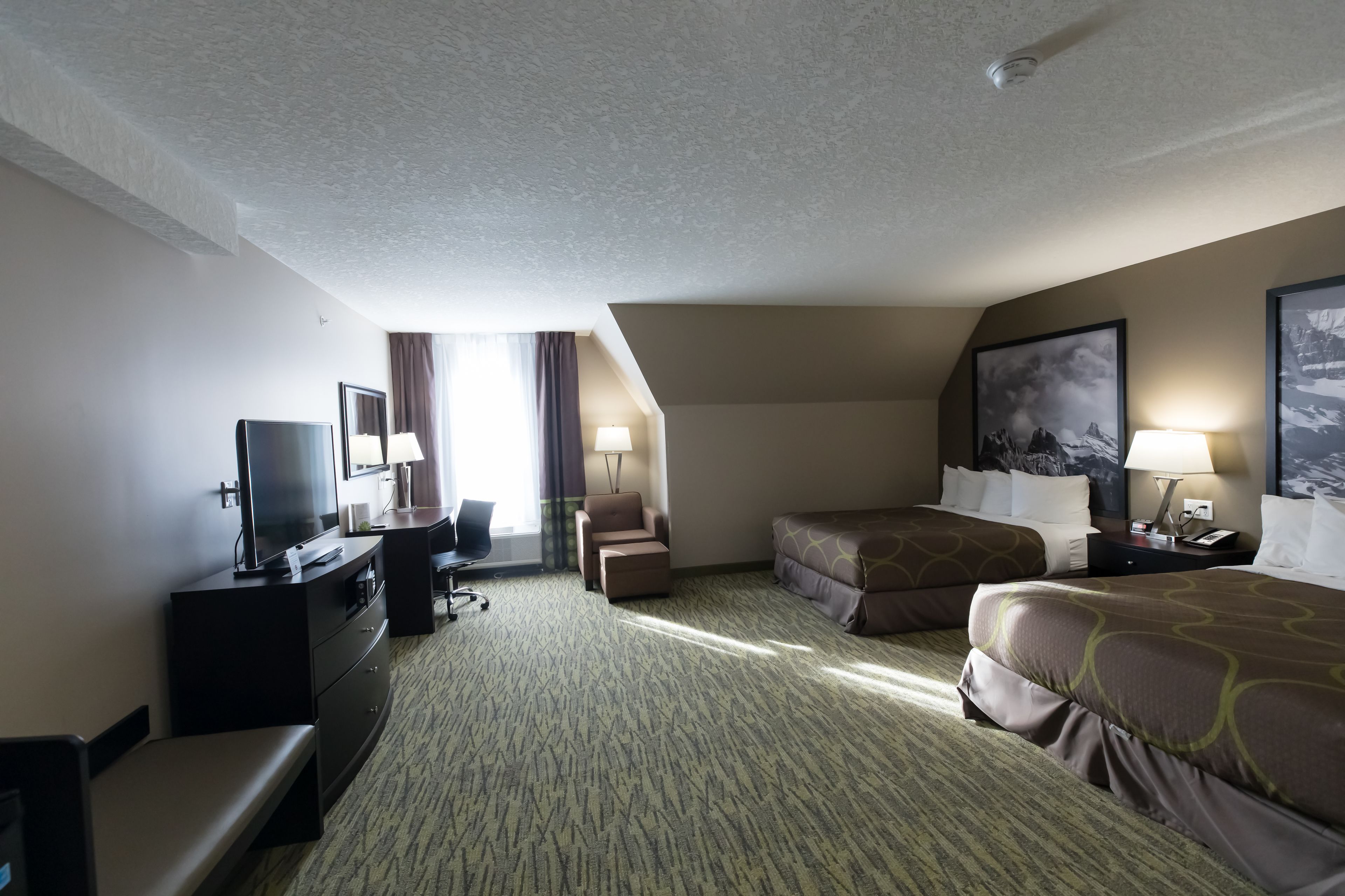 Quarto de hotel com televisão de tela plana, escrivaninha, duas camas, sofá e uma janela grande com cortinas.