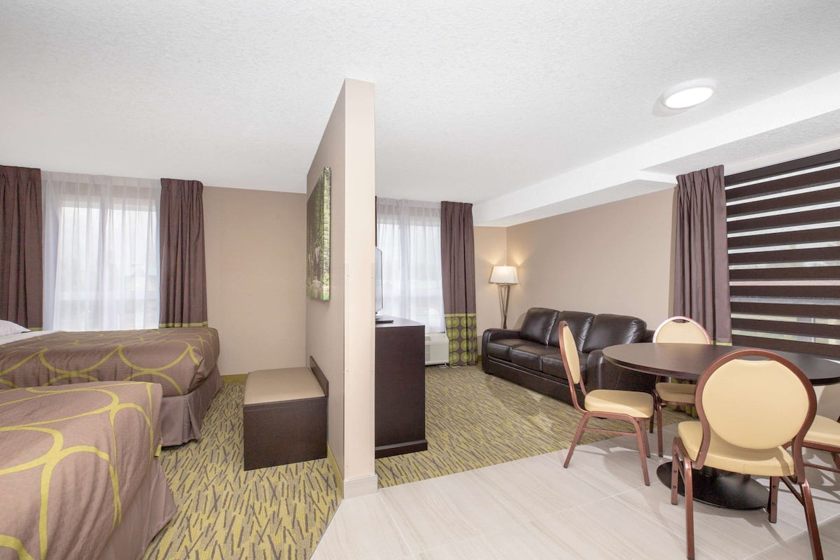 Quarto de hotel com duas camas, um sofá, uma mesa de jantar com cadeiras, uma escrivaninha e um abajur.
