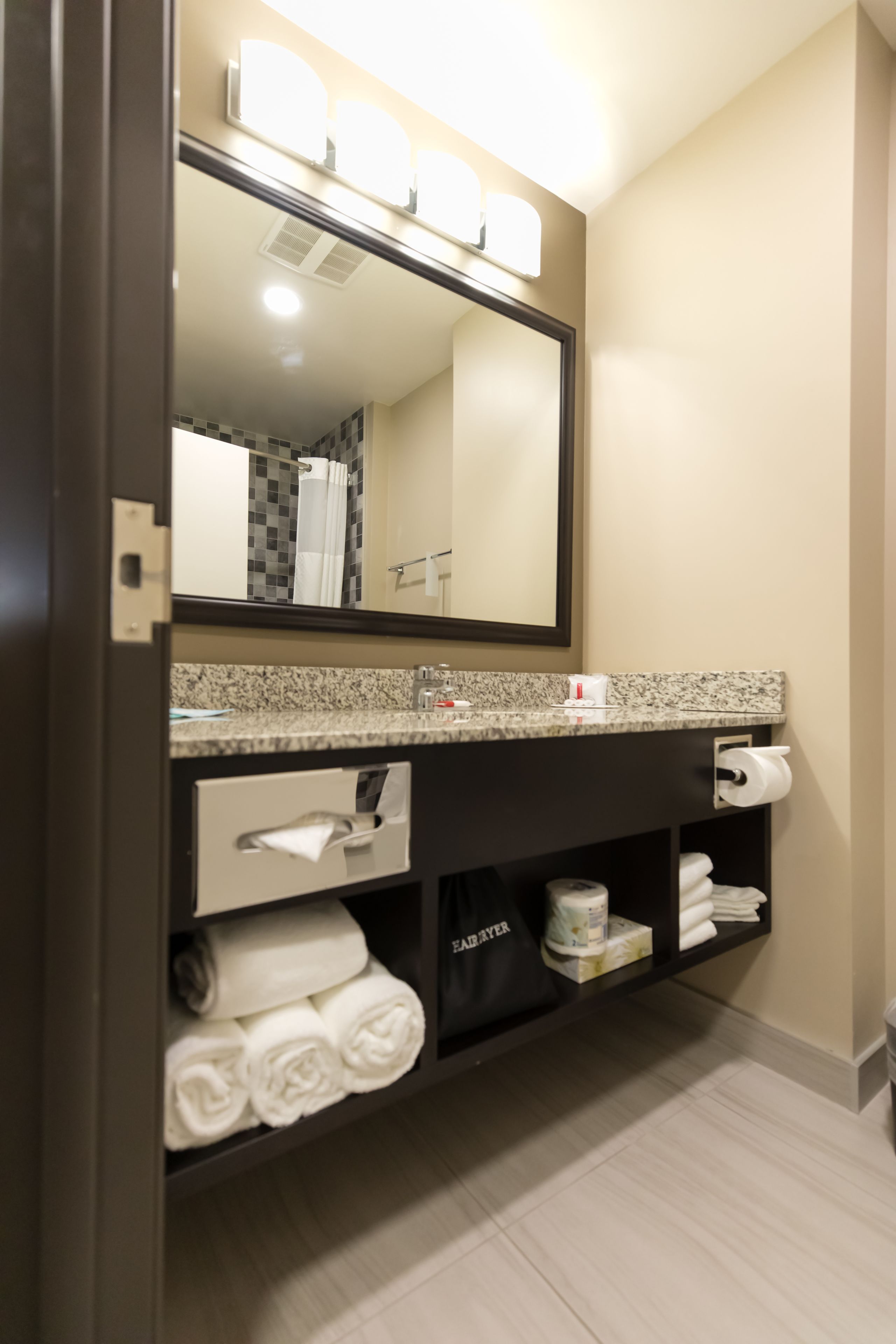 A modern bathroom with a granite countertop, a large mirror, and a towel rack.