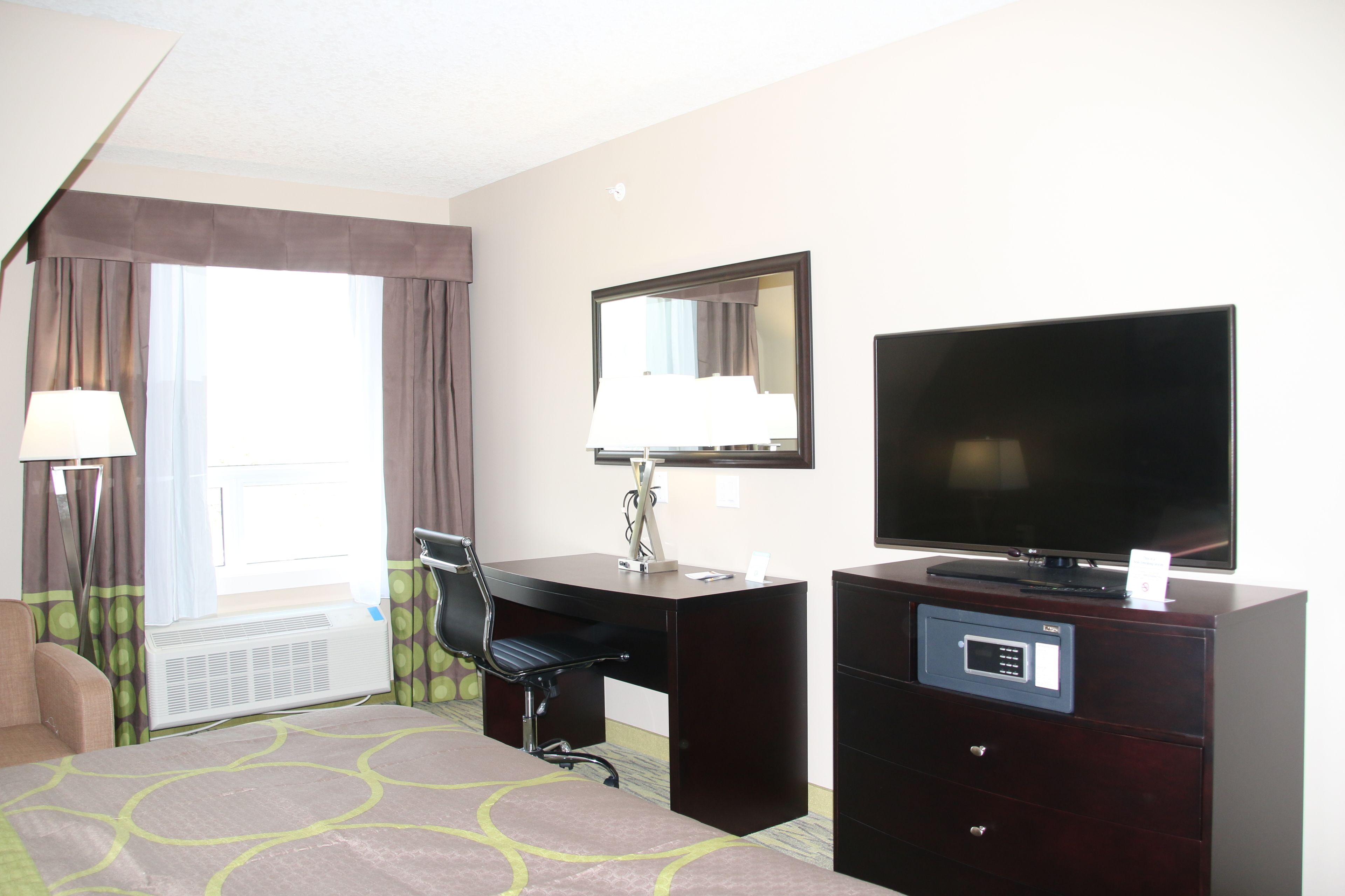 Une chambre d’hôtel avec un lit, un bureau, une chaise, une télévision et une fenêtre avec des rideaux.