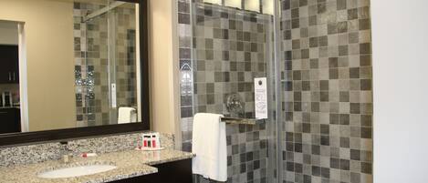 A bathroom with a granite countertop sink, a mirror, a glass shower enclosure, and a tiled shower wall.